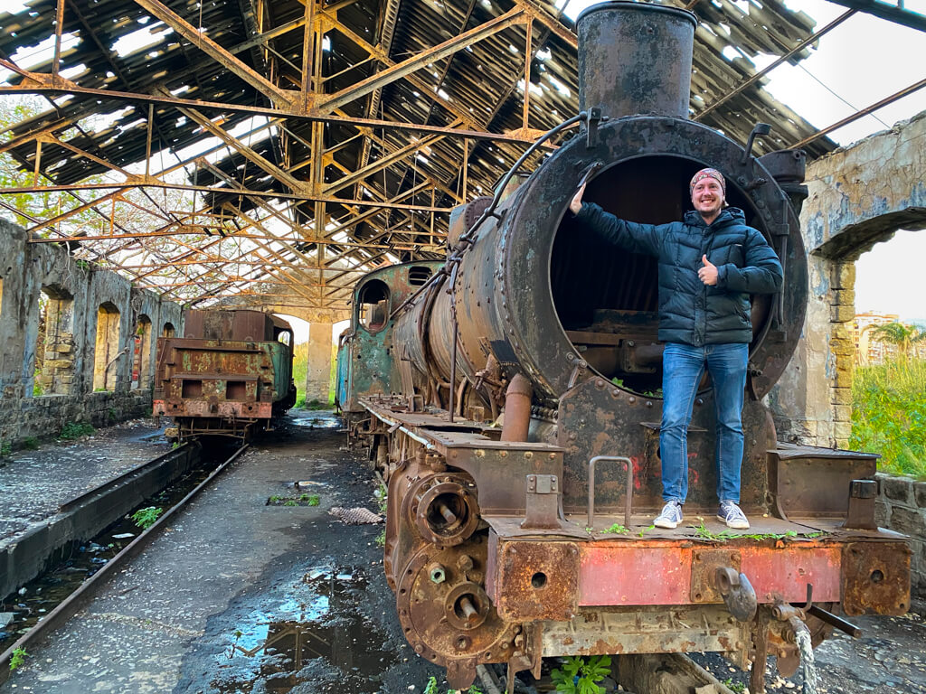 Me, standing on the front of a locomotive in a run down railway building.