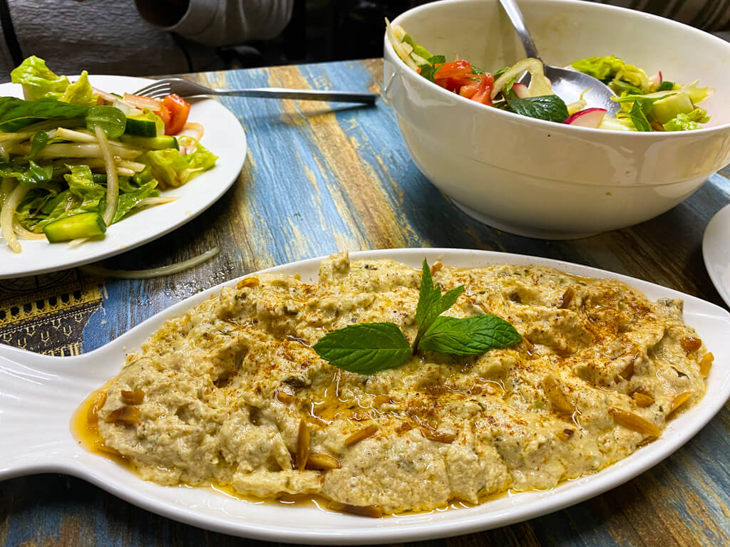 A plate of fish with Tahini with two plates of salad in the background.
