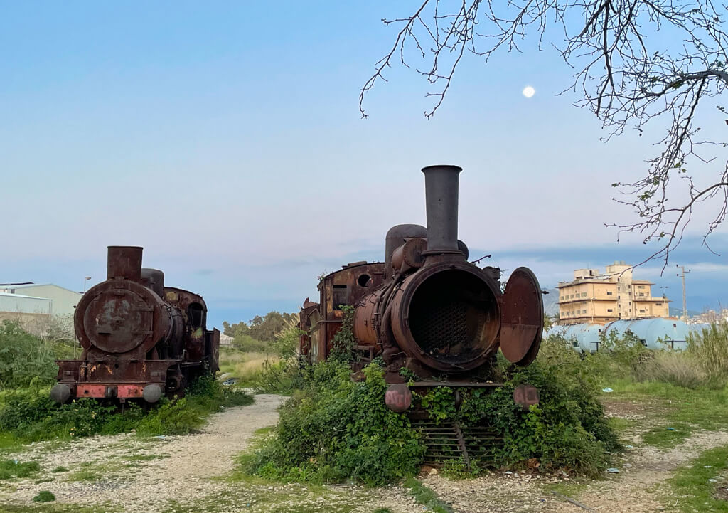 Two old locomotives rusting outdoors under the moon at dusk