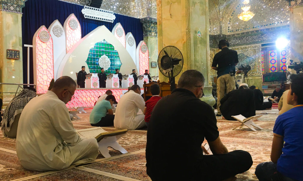 Religious figures reading prayers in the Al-Askari mosque while people pray.  