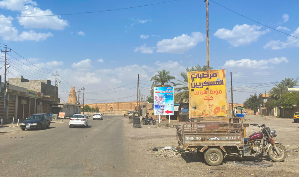 A random road with an old motorbike cart parked on the side with the Malwiya minaret in the background.  