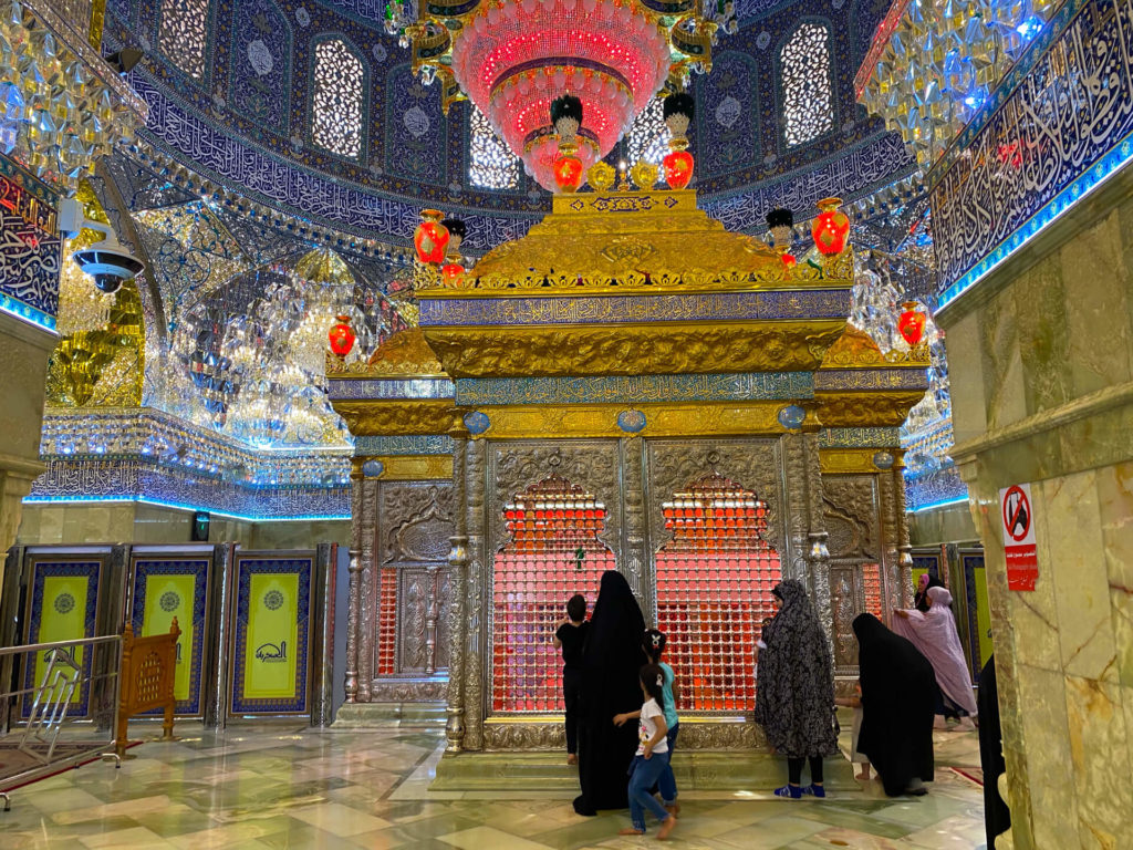 Women walking through the colourful interior of the mosque past the tomb of an imam.