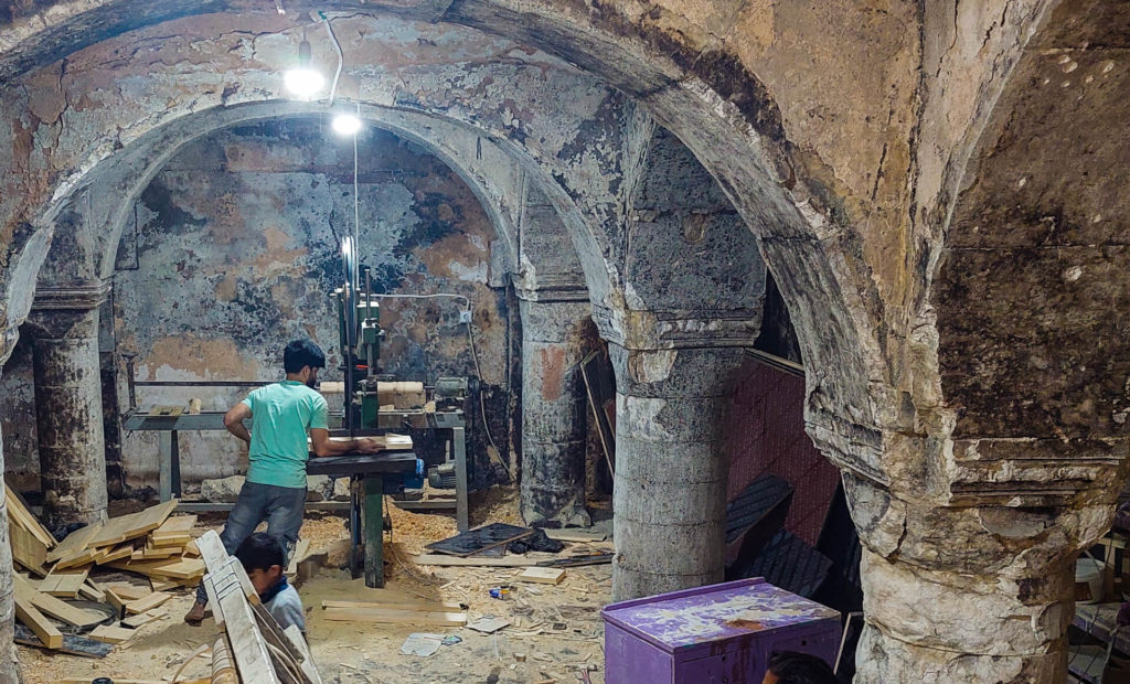 A boy using an electric saw to cut wood in a basement.