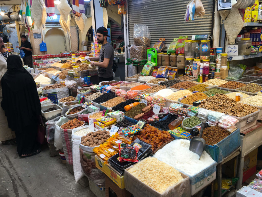 A vendor selling spices talks to an Iraqi woman in full abaya next to his colourful wares.