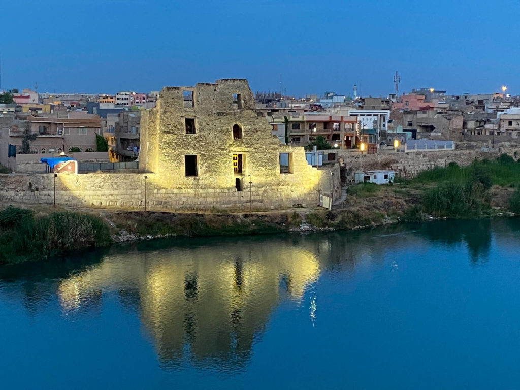 A historic-looking building lit up by the banks of the Tigris.