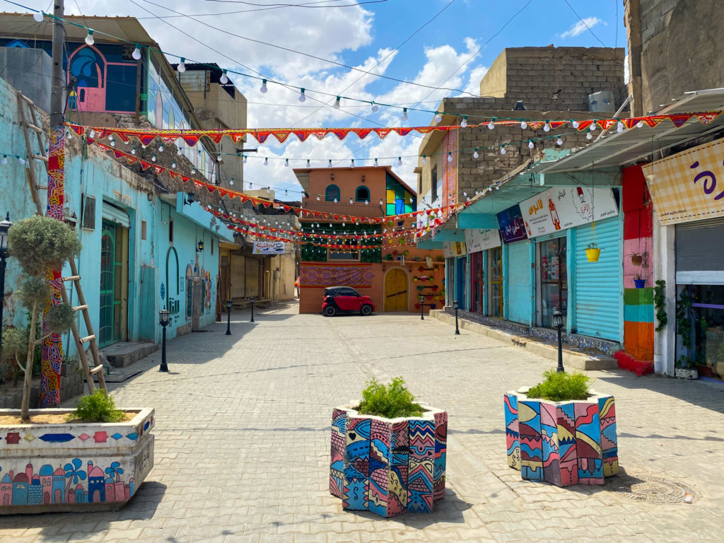 A brightly coloured street in Mosul with blue walls and red bunting hanging across the street.