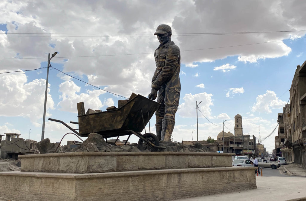 A metal statue of a construction worker with a wheelbarrow full of rubble.