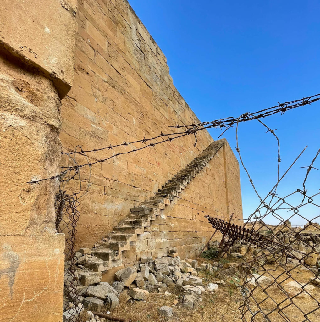 A staircase runs steeply up the side of the ancient walls of Hatra with barbwire in the foreground.