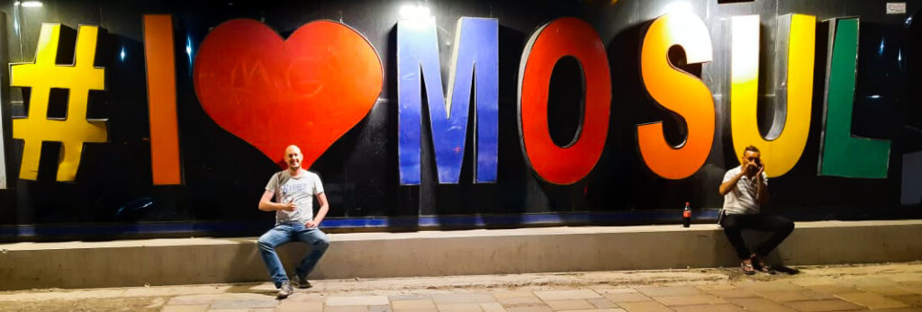 The I Love Mosul sign, with each letter in different colours, and me and a random guy sitting in front.