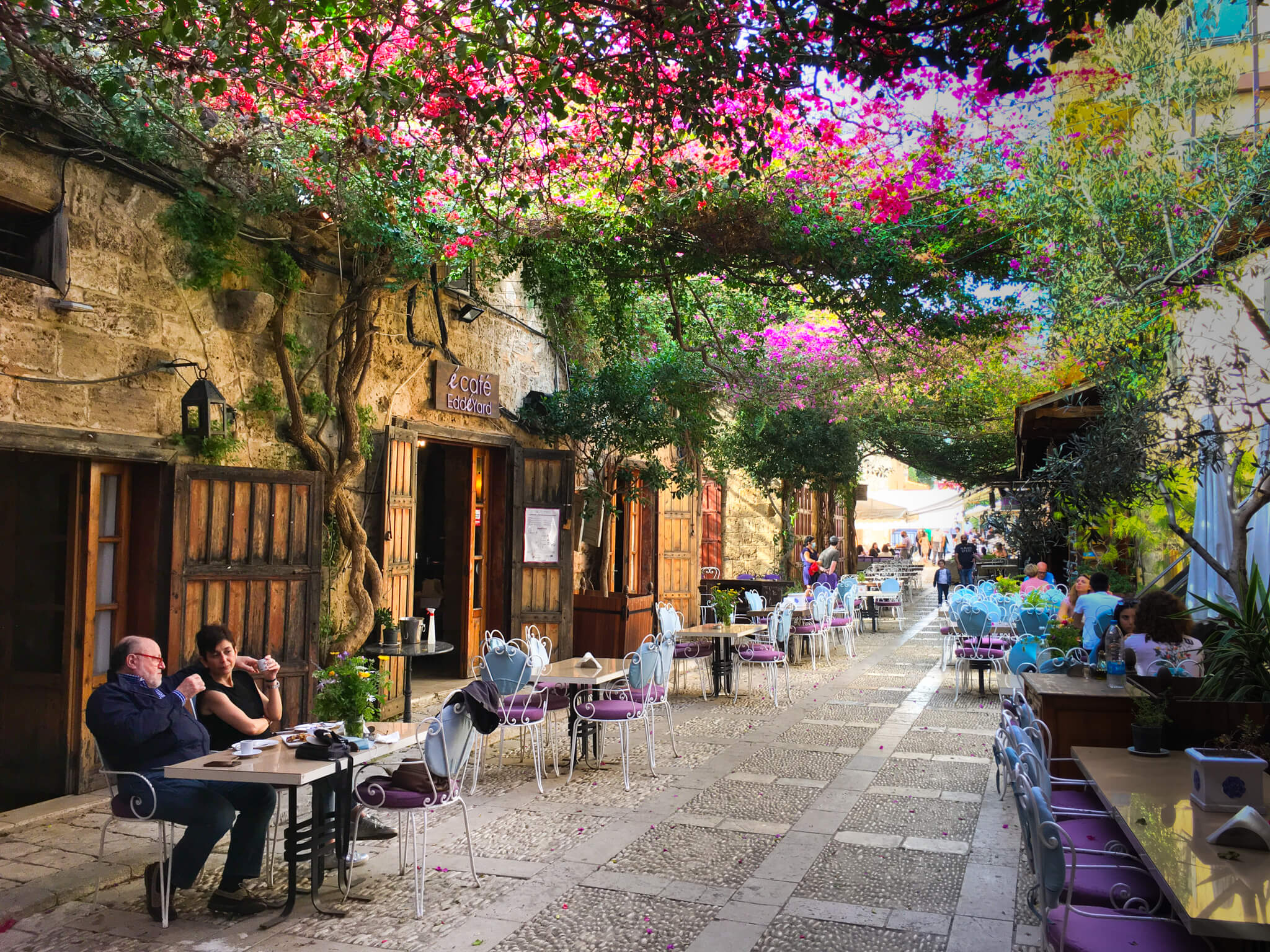 A local restaurant with tables outside on the street and flowers growing above.