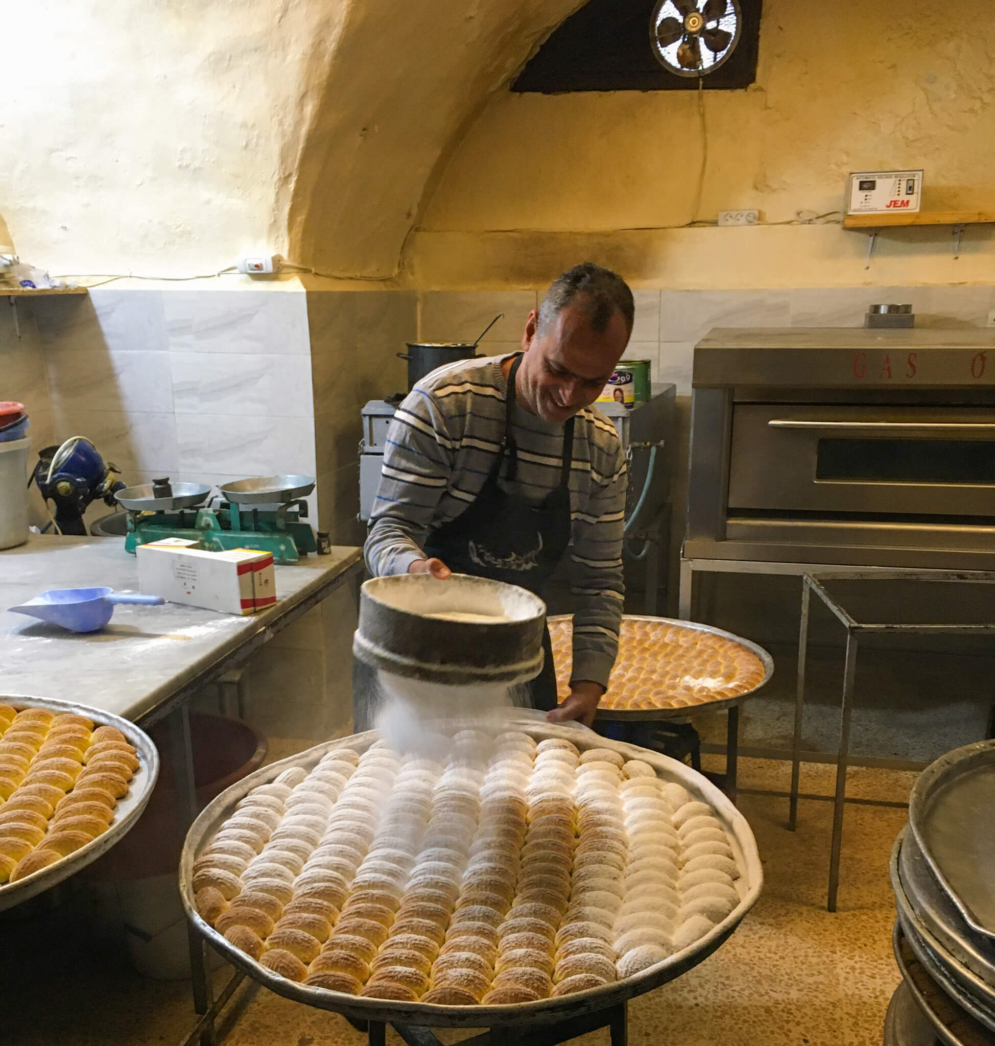 A man sieving icing sugar over Arabic sweets