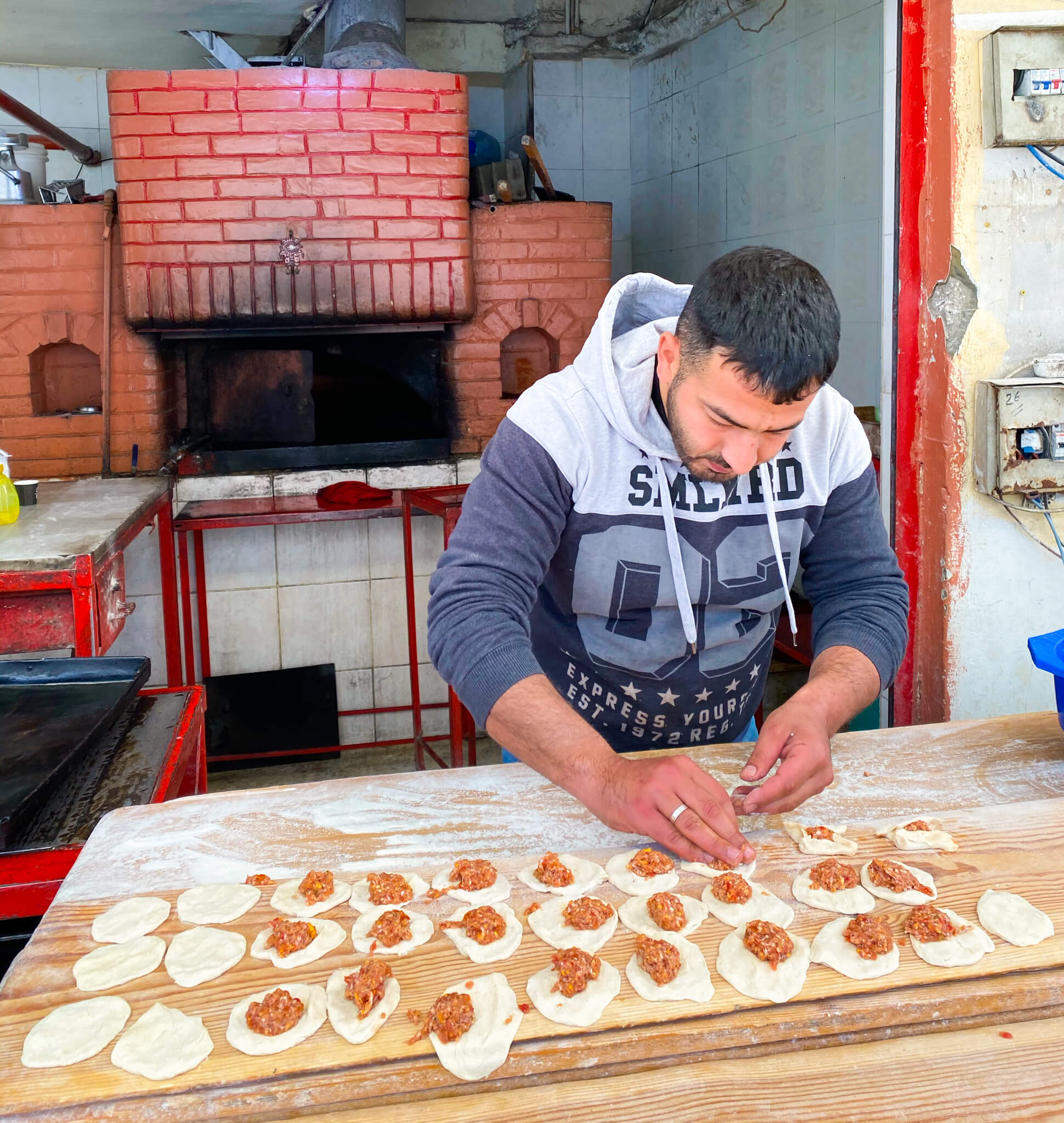 A local man filling sfiha pastries with minced meat in front of a brick oven on the edge of the street in Baalbek