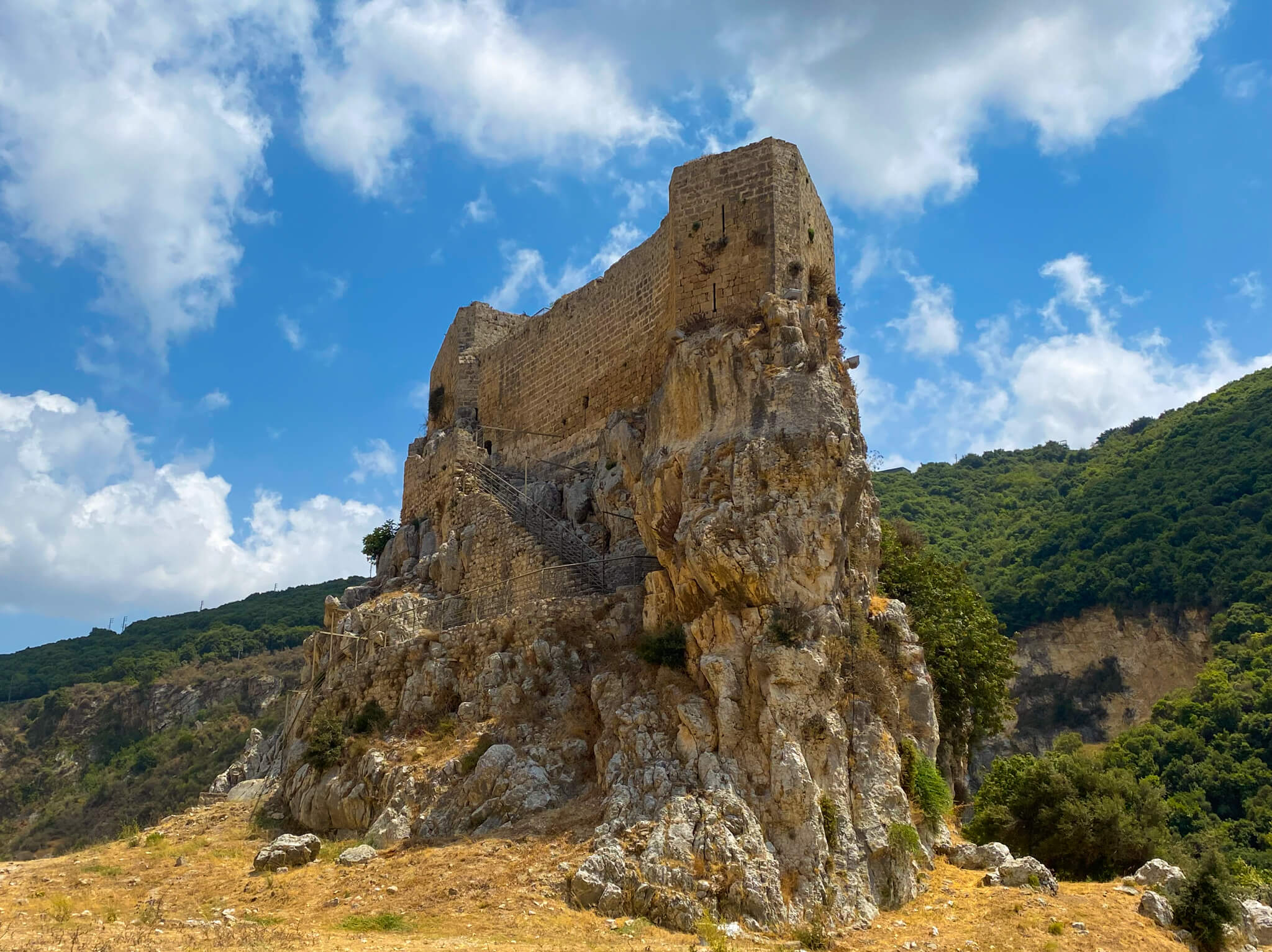 Mseilha Fort, perched on a rock with green hills and blue skies in the background.