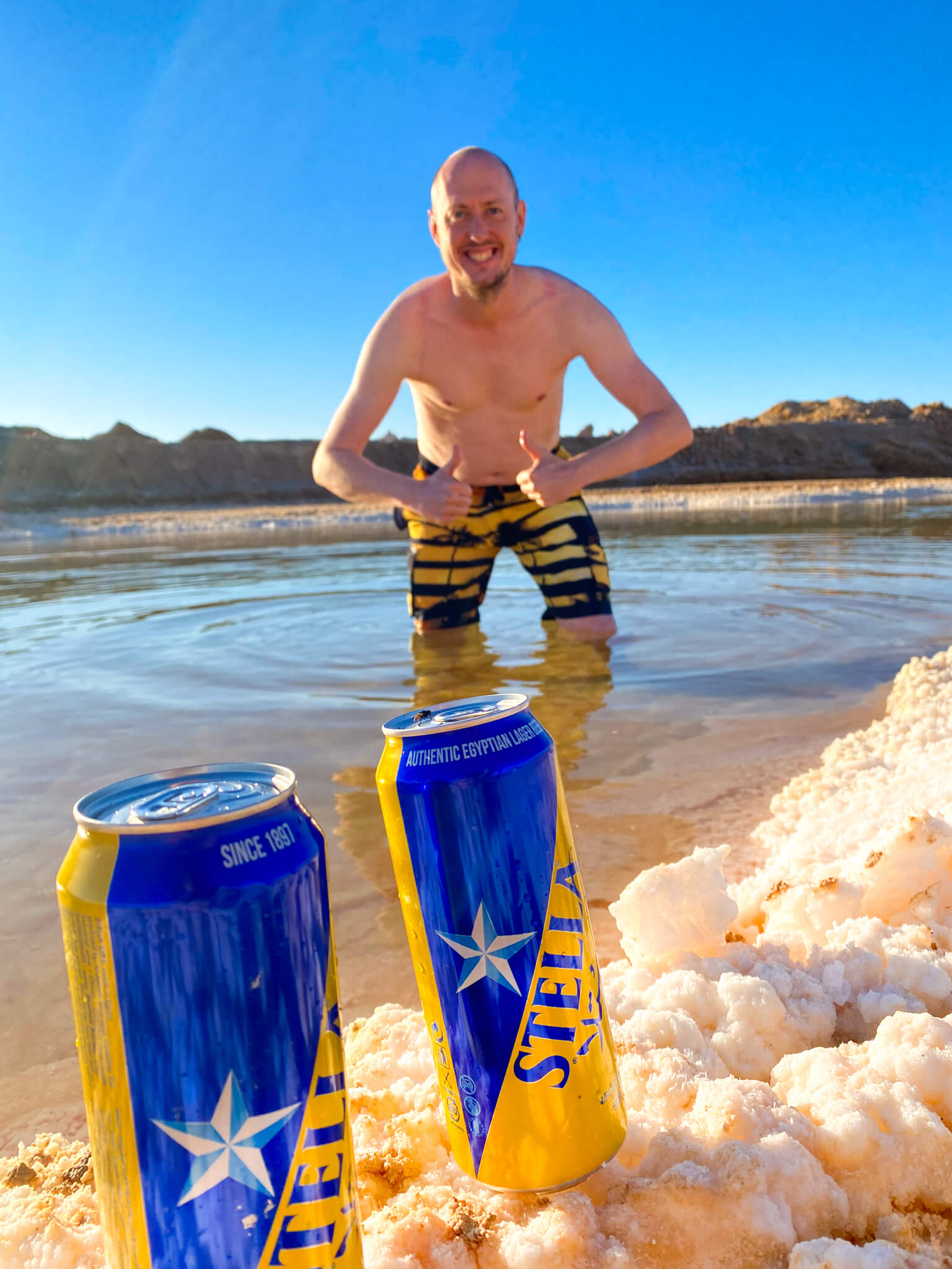 Two cans of beer marked Stella, but with a different logo to the Belgian beer, with me in the salt pool behind