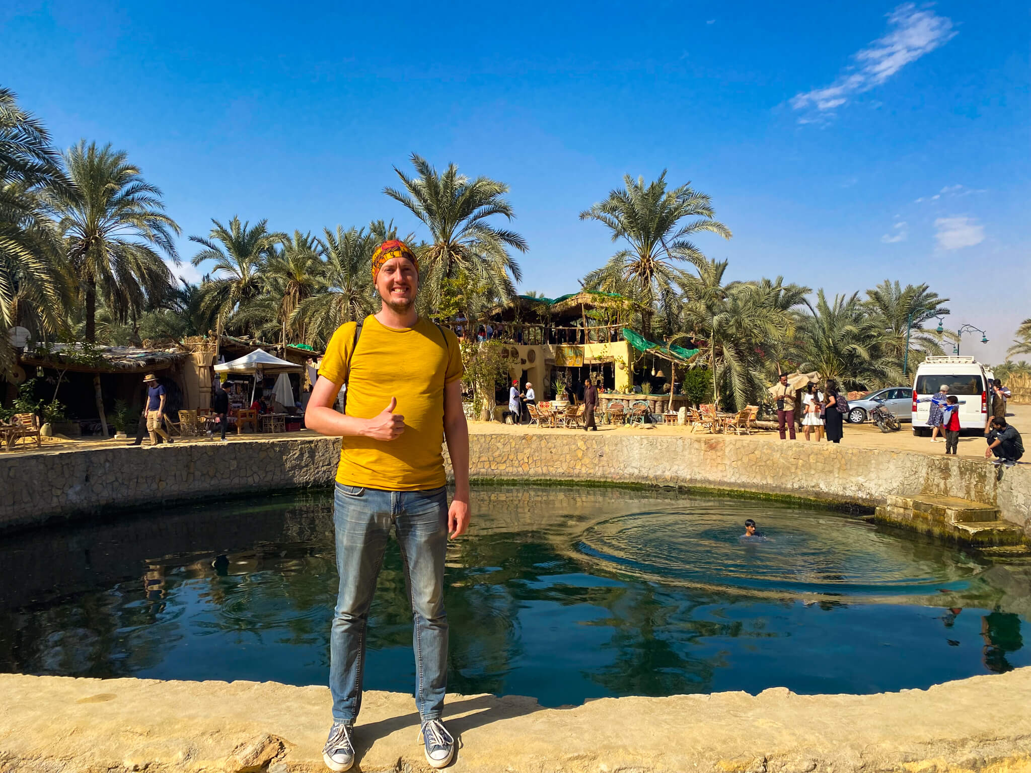 Me, standing in front of a concrete pool with rubbish floating in it and palm trees in the background.