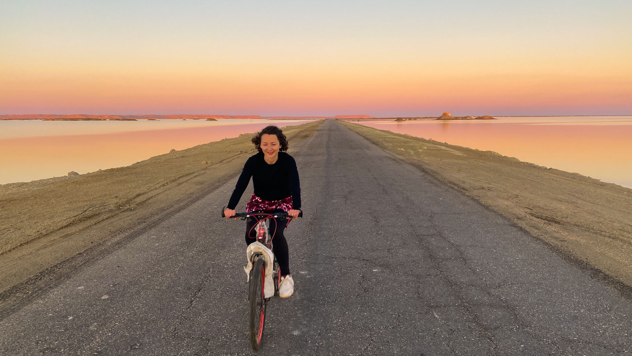 Anna cycling with the pink sky and lake in the background.