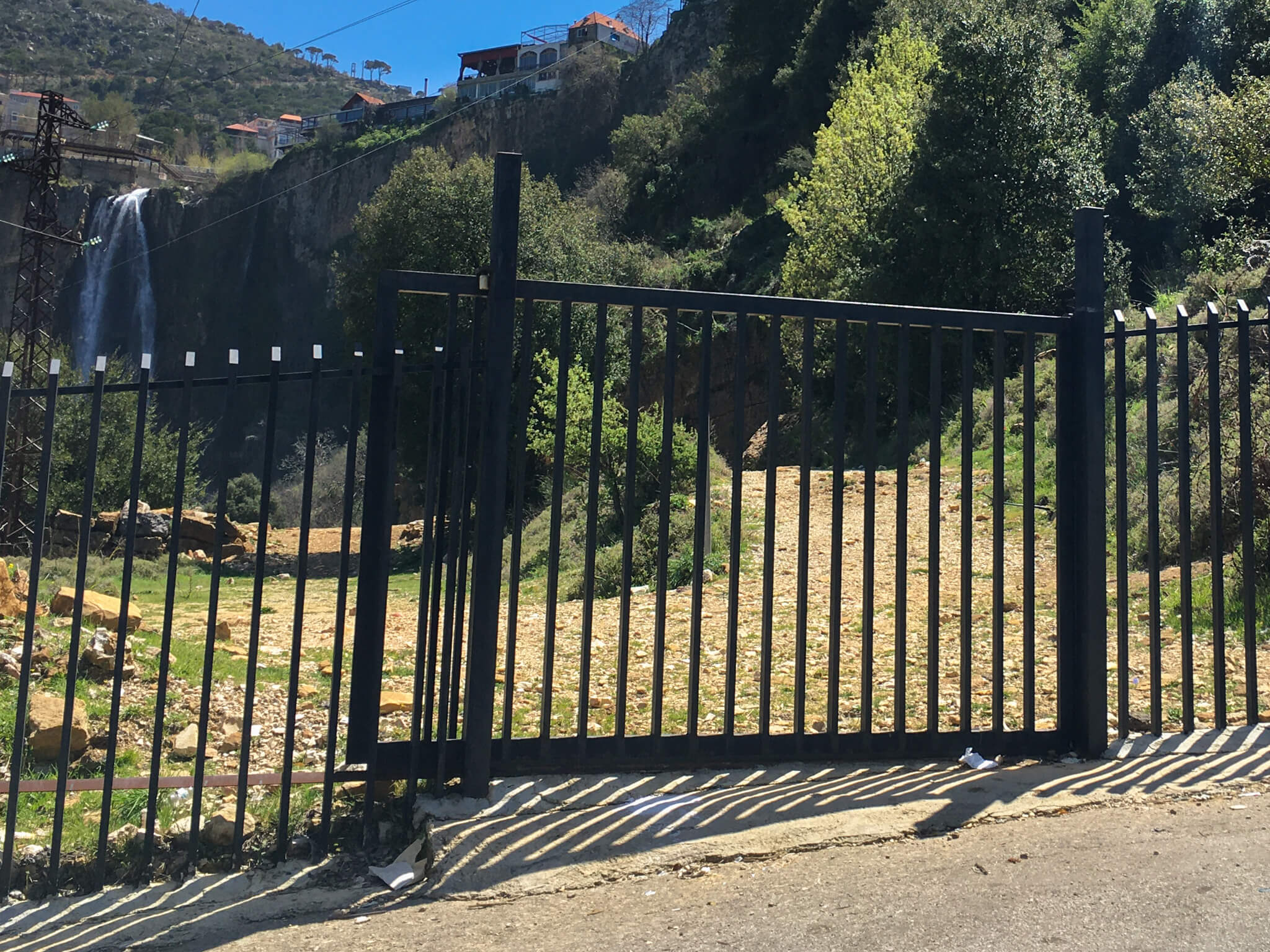 A modern metal gate about 2m tall with the waterfall in the background behind it.