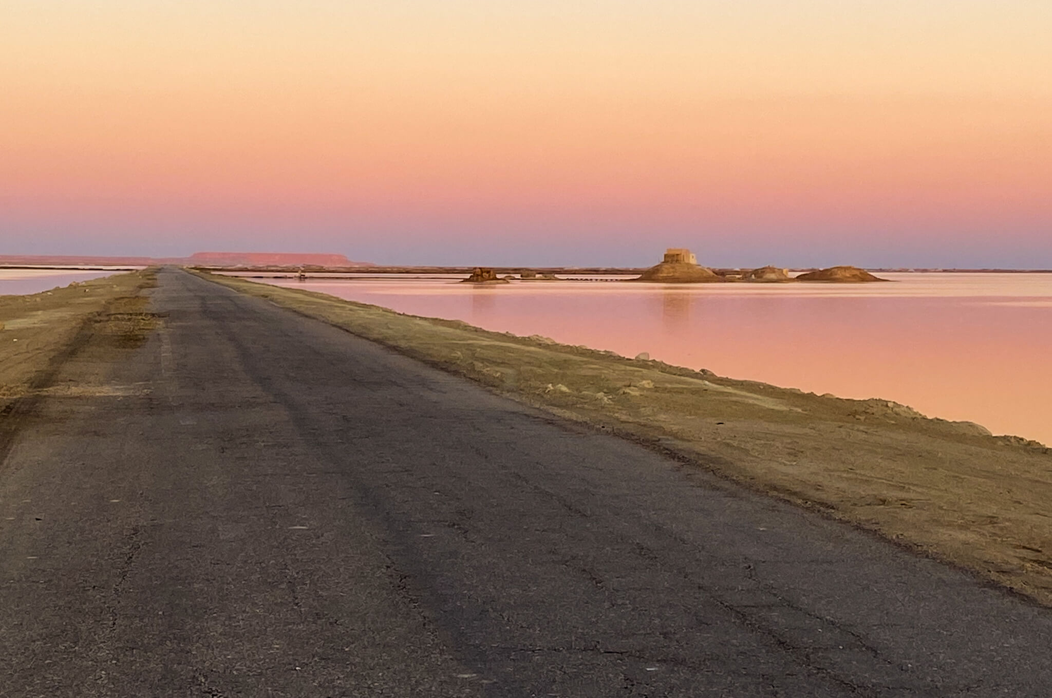 Pink skies over a lake of the Siwa Oasis with a string of islands next to the long straight road.