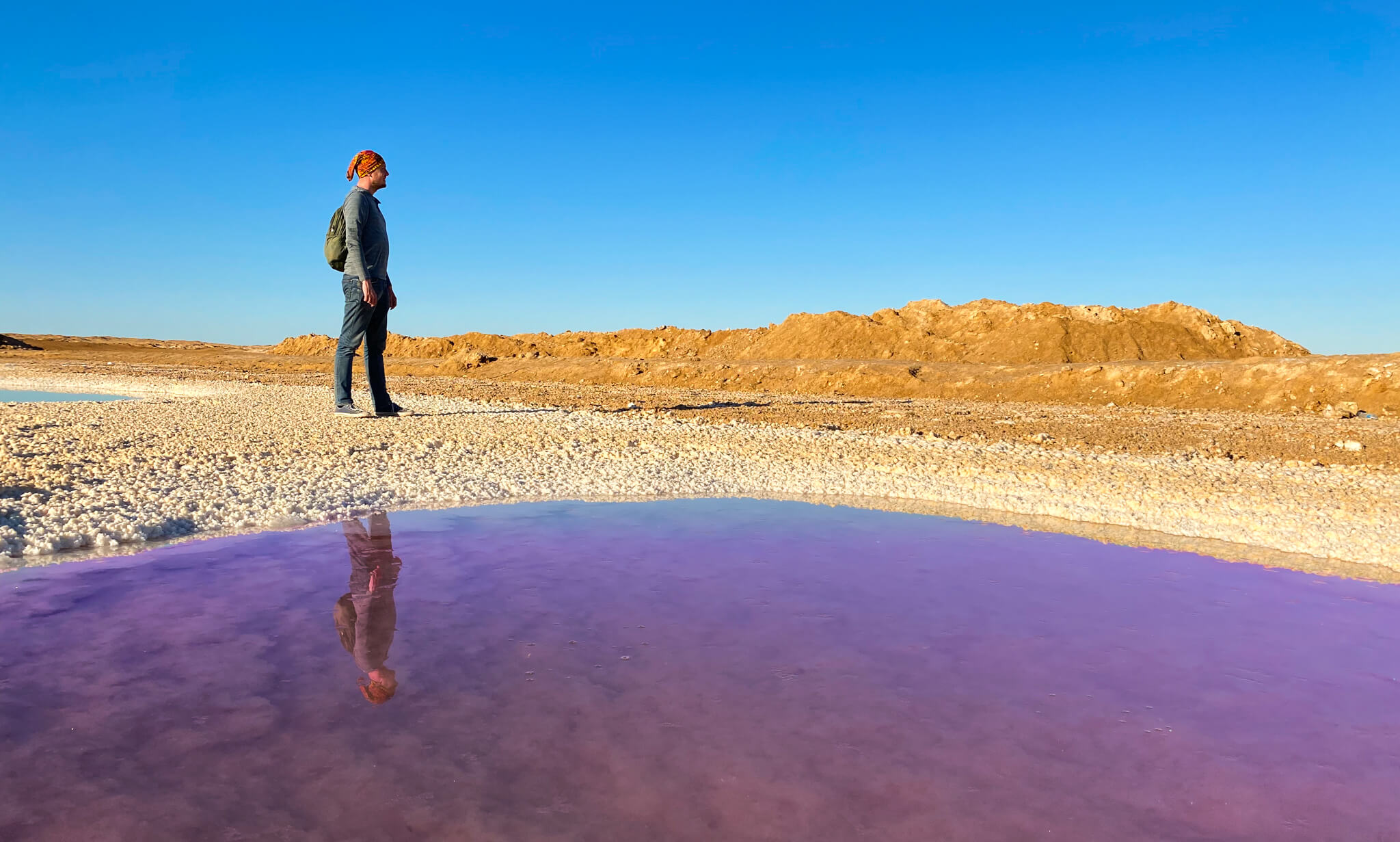 Me standing next to a salt pool with my reflection in the purple-coloured water