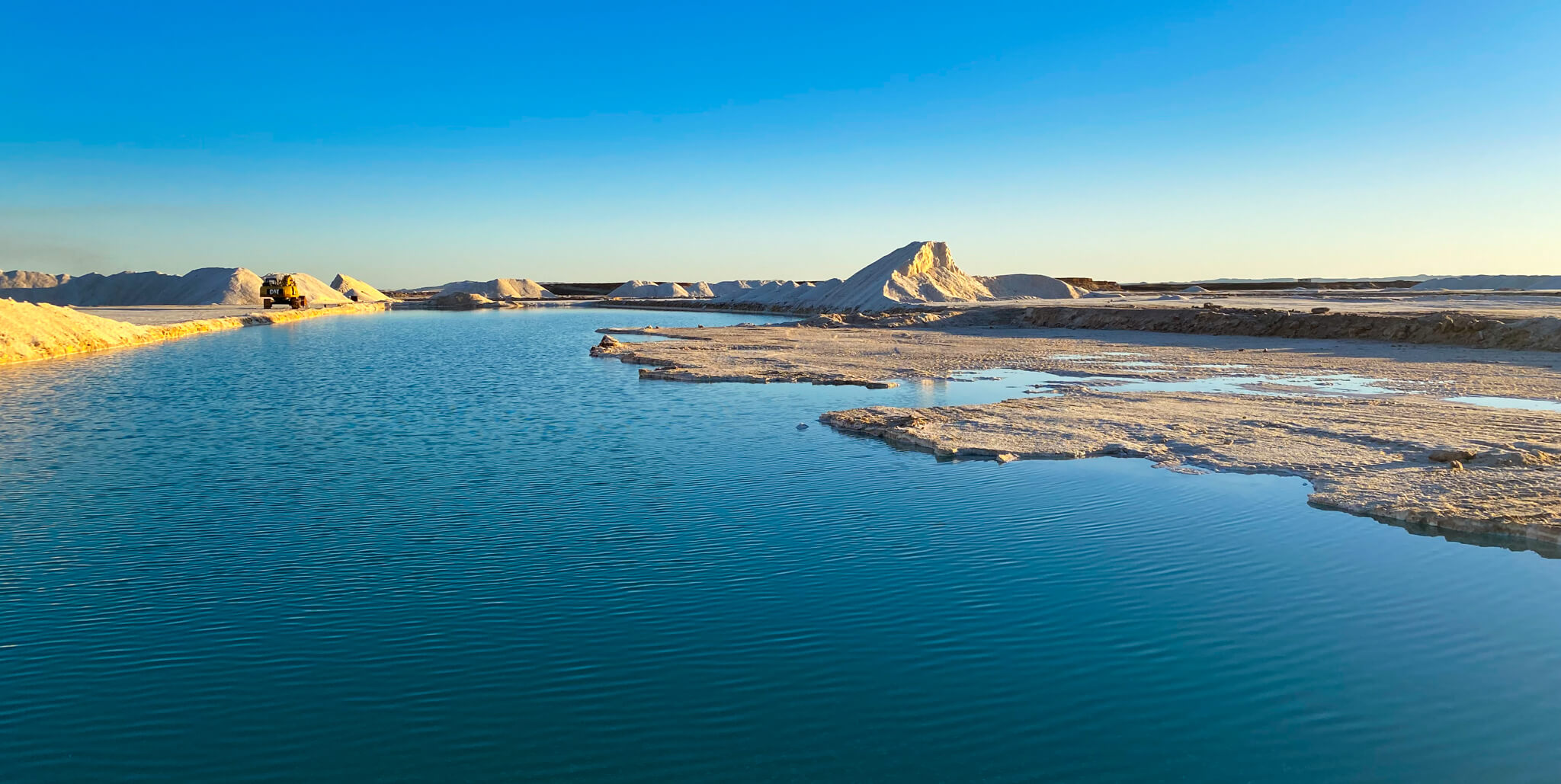 Deep blue salt lake with mounds of salt in the background.