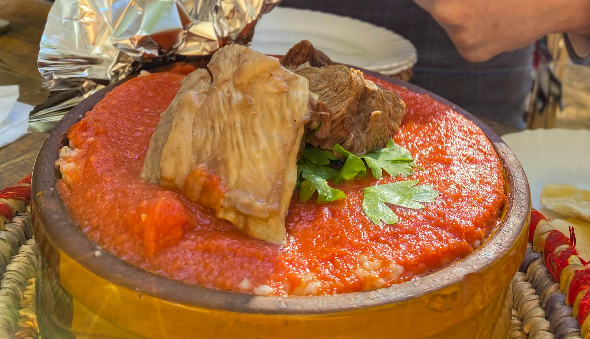 A bowl of bright red camel stew with large pieces of meat on top.