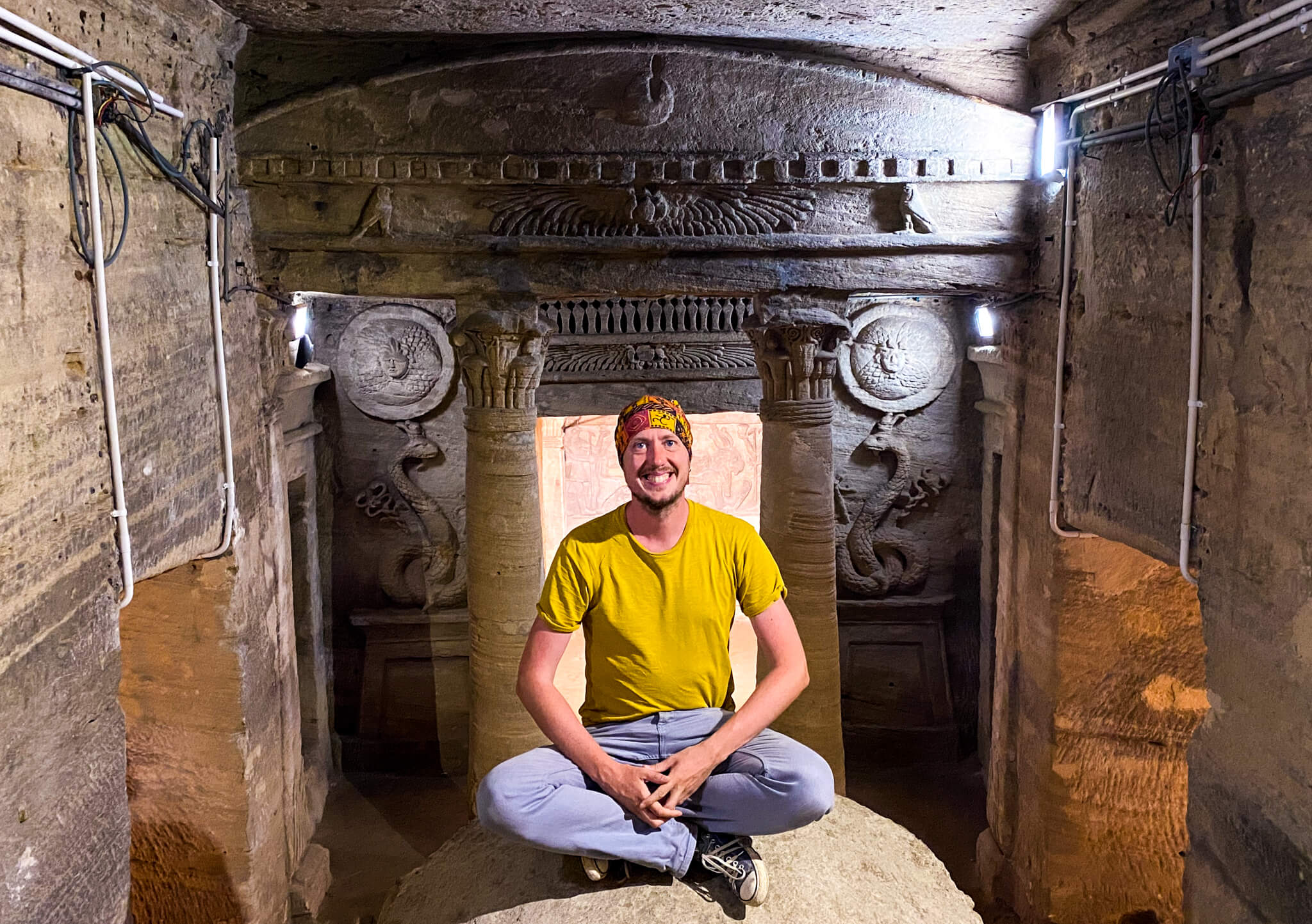 Me sitting on a rock with a beautiful carved wall of the catacombs behind me.