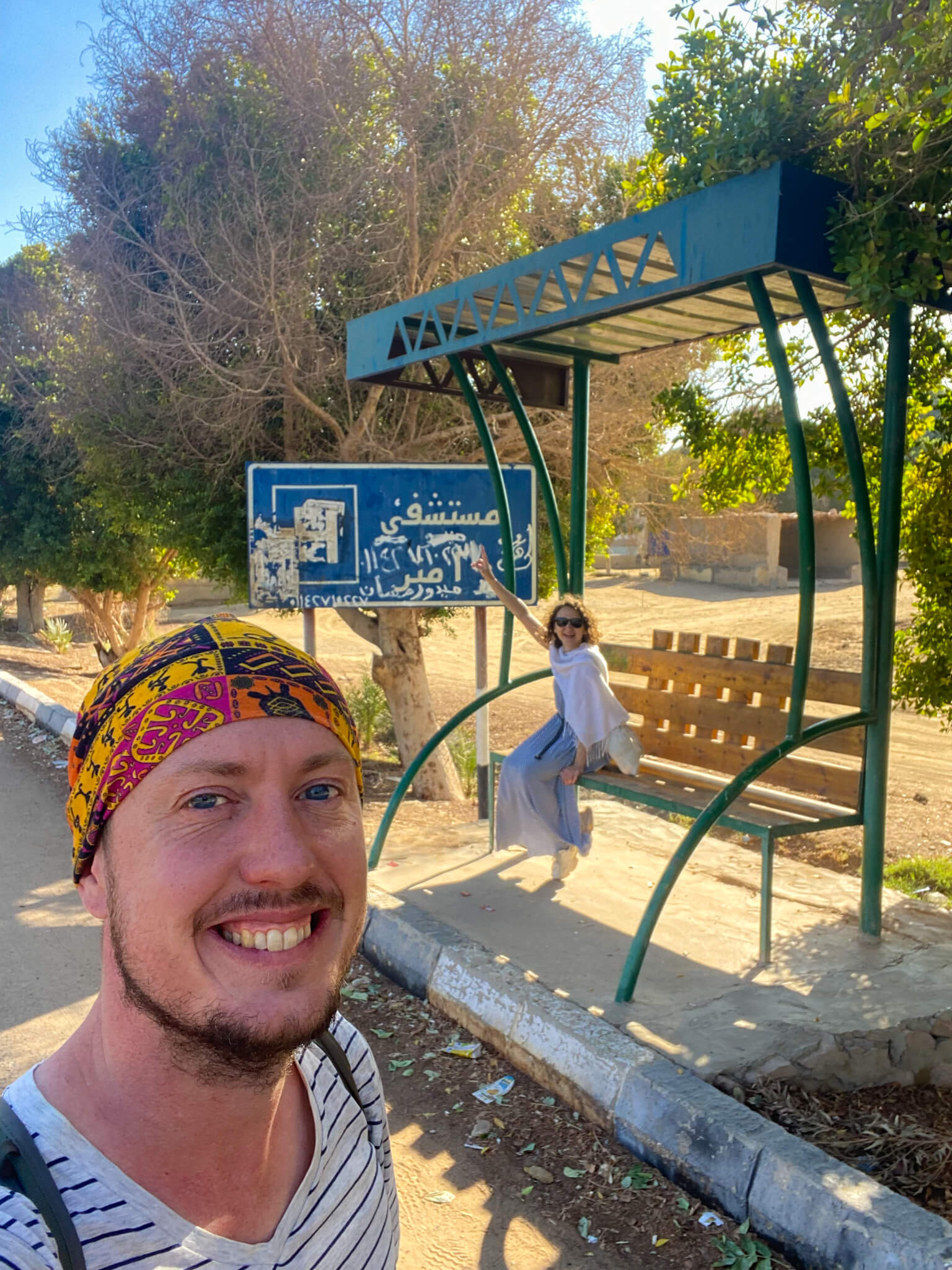 Anna waving from a metal bus shelter waiting for the bus back to the Tombs of the Nobles.