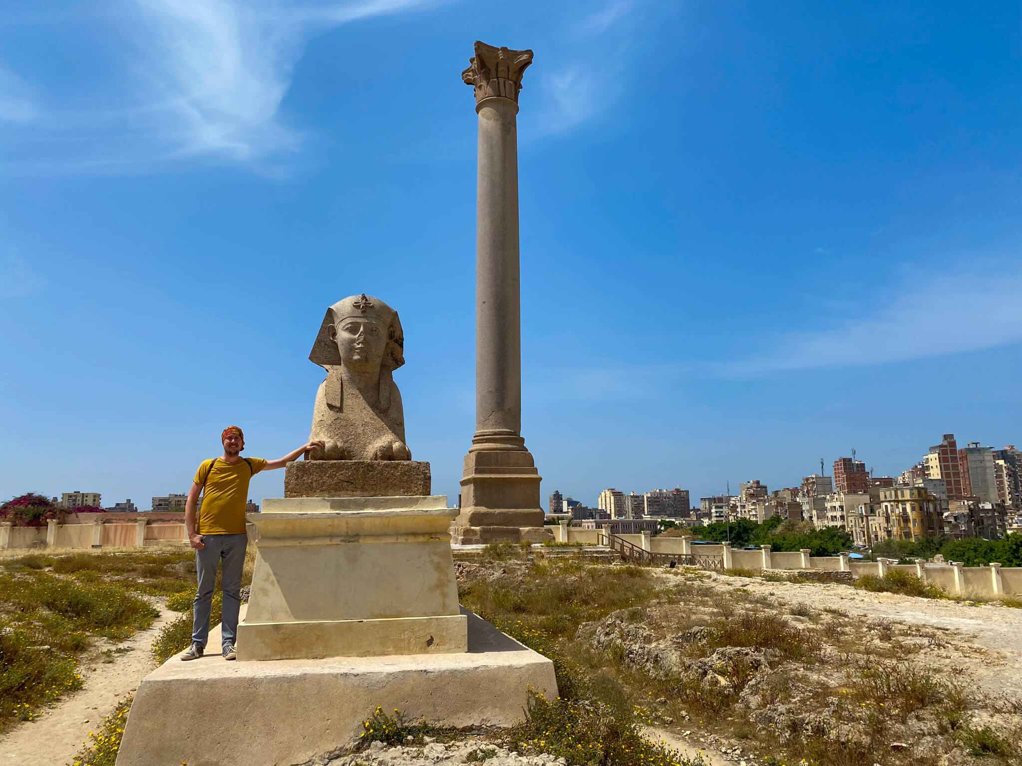 Me, leaning against statue of a sphinx with Pompey's Pillar and a lot of apartment blocks in the background.