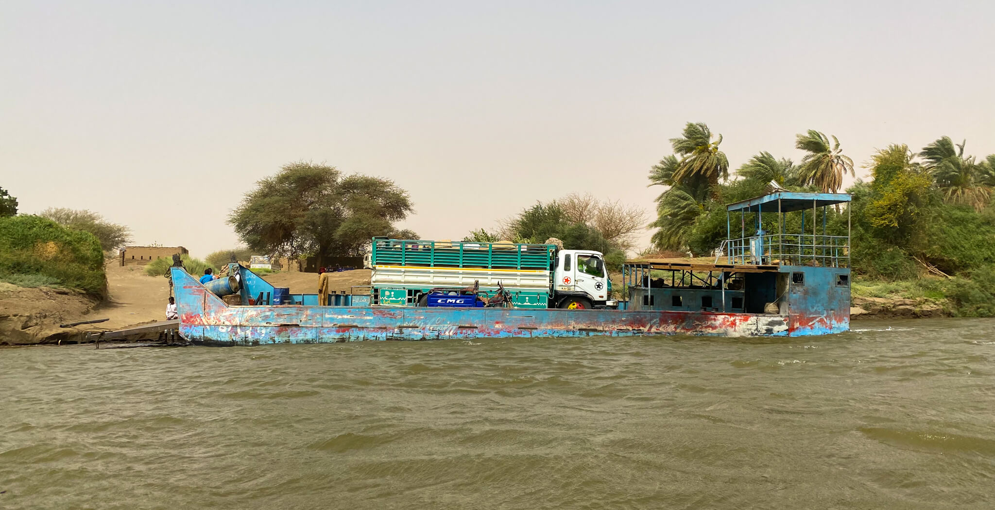 A blue ferry docked at the bank of the Nile on Sai Island.