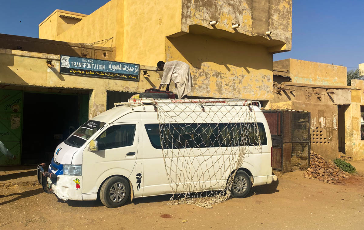 A minibus with a man standing on top preparing to load bags onto the roof.