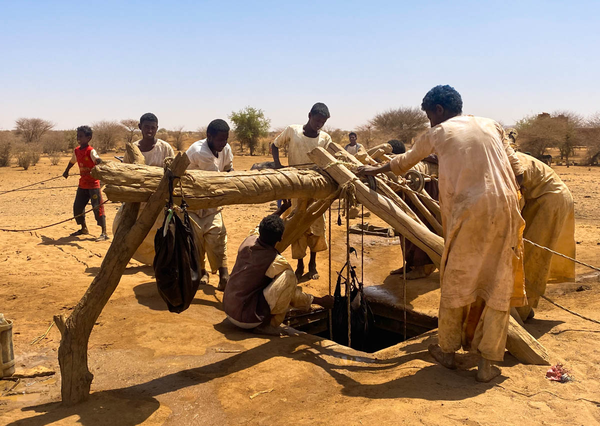 Local men clustered around a well with a wooden contraption over it to hang water pouches.