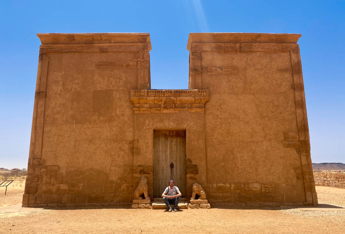 I sit between two lion statues missing heads at the entrance to the Apedemak 