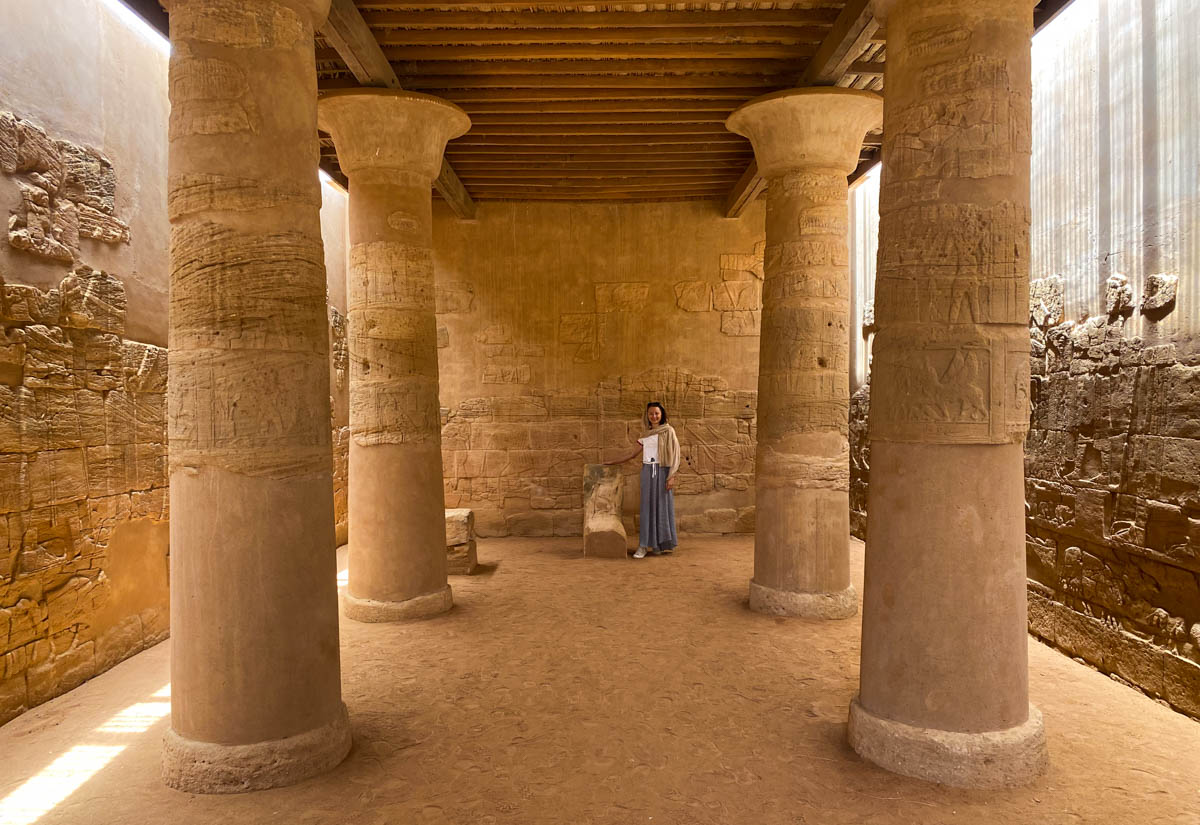 Anna standing next to the altar inside the Apedemak with four monolithic columns in the foreground.