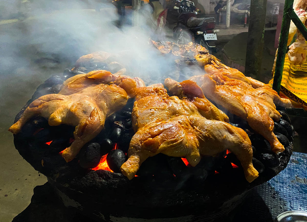 Whole chickens cooking over charcoal.