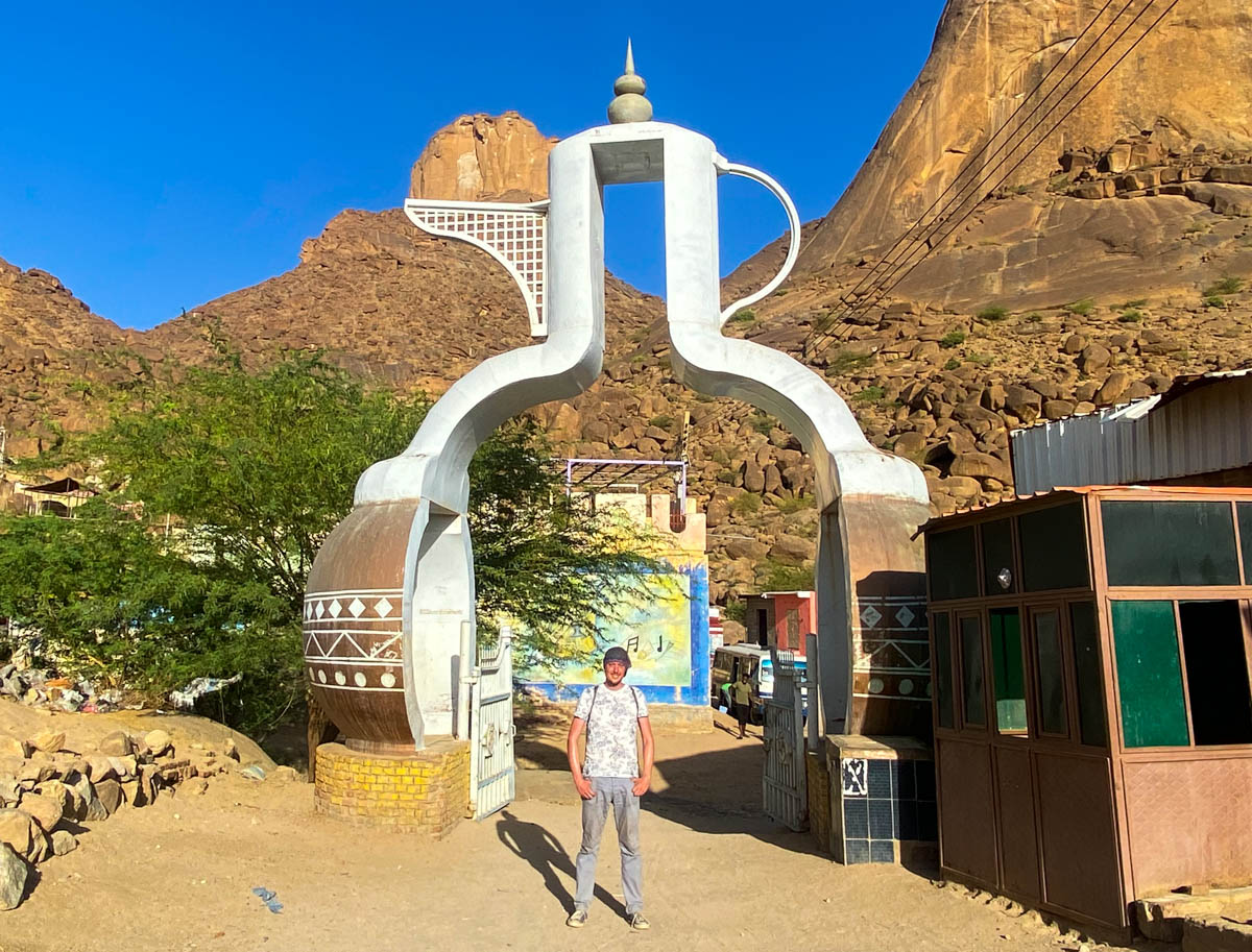 Me standing under an archway shaped like a traditional pottery coffee pot.